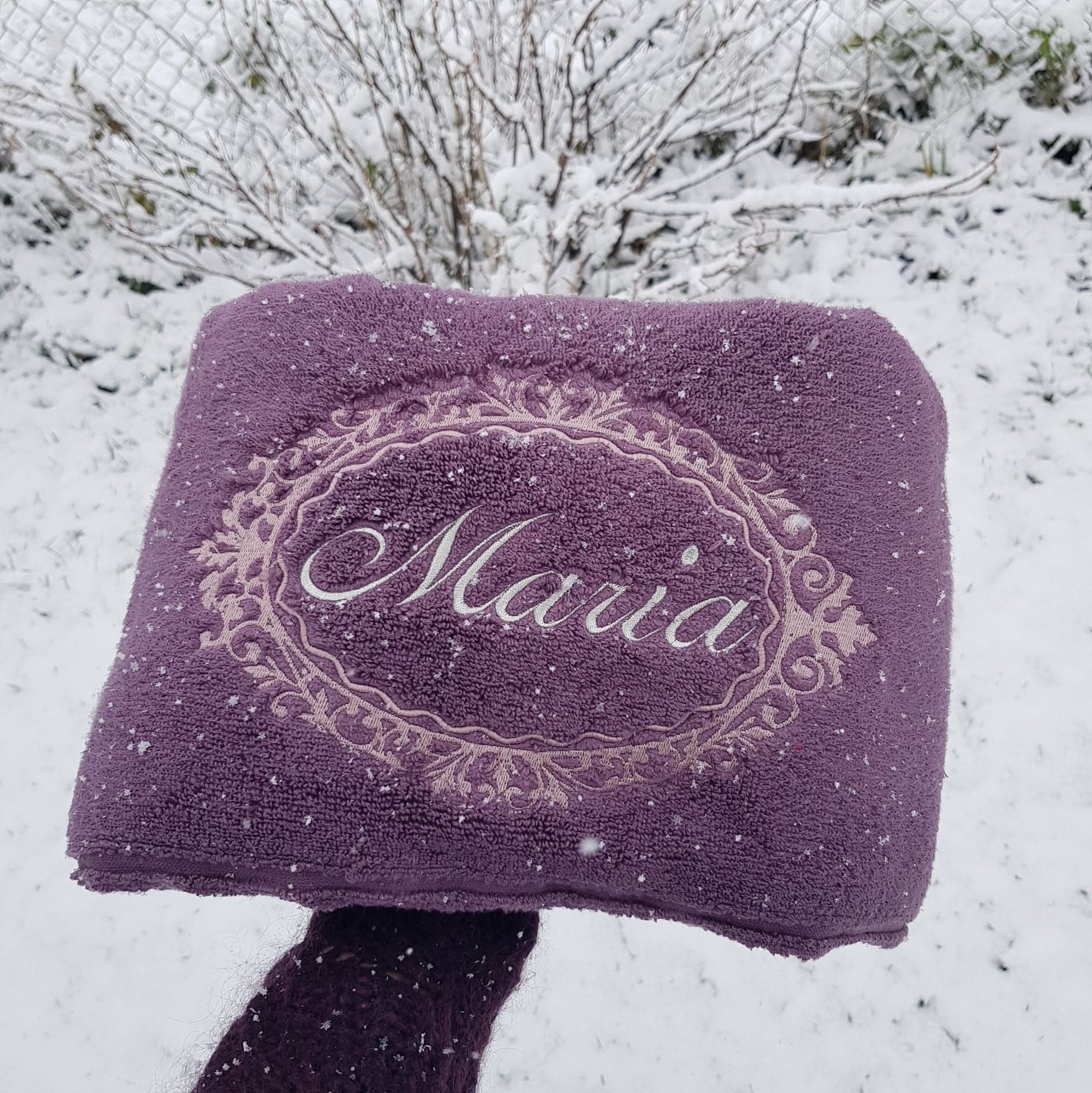 Fioletowy ręcznik z wyhaftowanym imieniem 'Maria' w ozdobnej ramce, prezentowany na tle zimowego krajobrazu w Szaflarach, pokryty świeżym śniegiem.