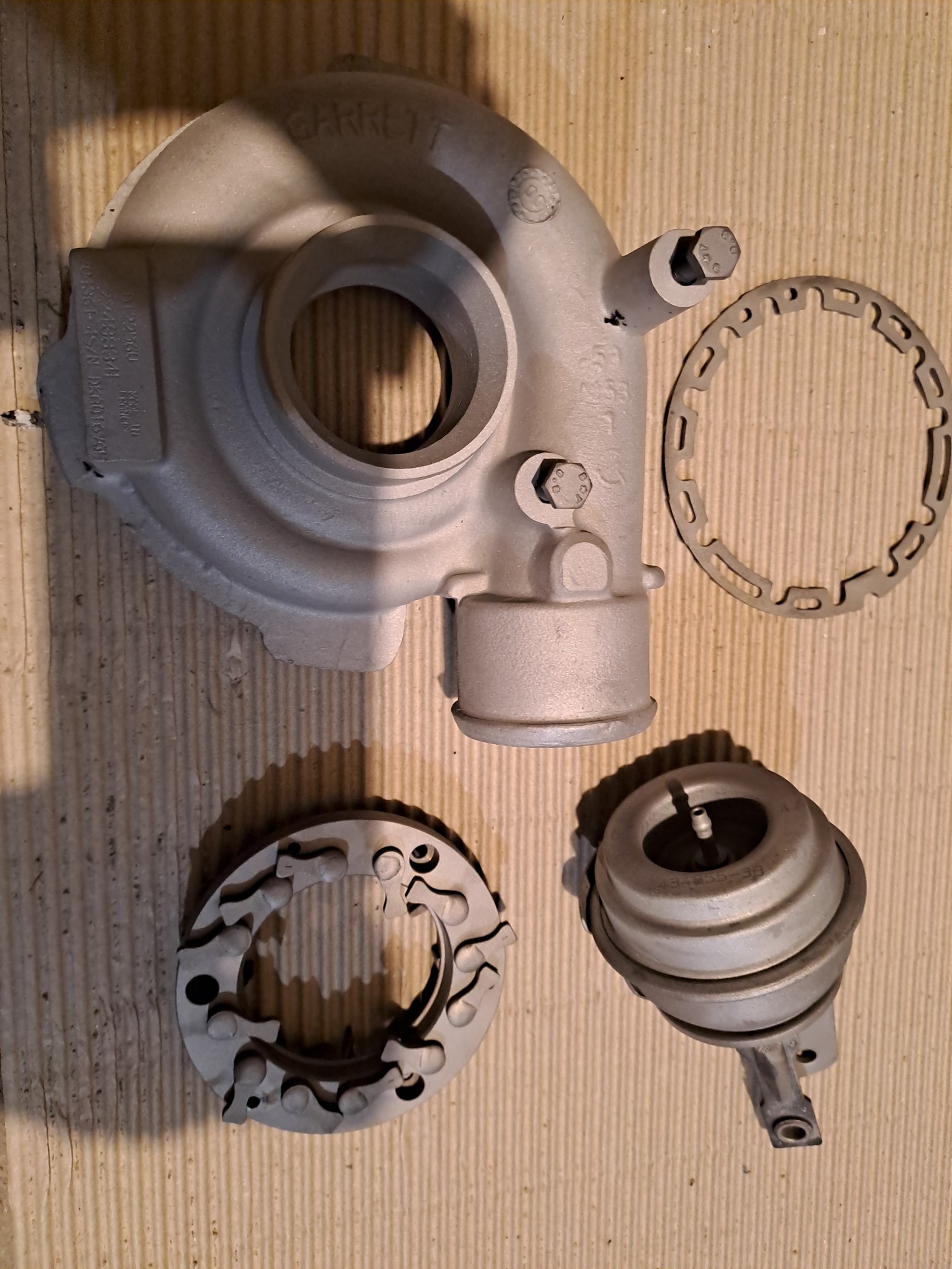 Elementy turbosprężarki Garrett po obróbce, leżące na tekturze, widoczne ślady po piaskowaniu.