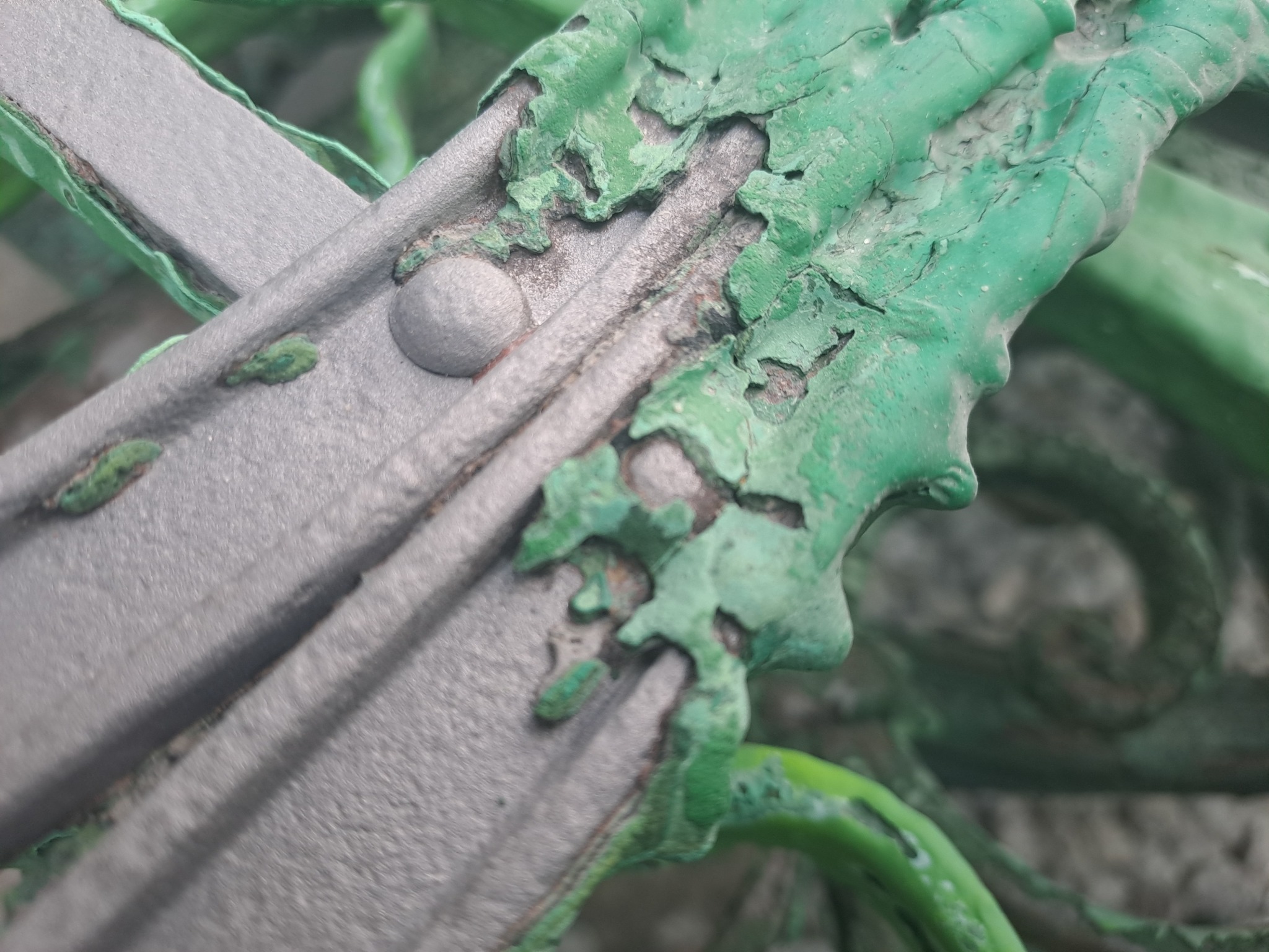 Zbliżenie na metalową konstrukcję z łuszczącą się, zieloną farbą, ukazującą proces korozji i odnowy powierzchni.