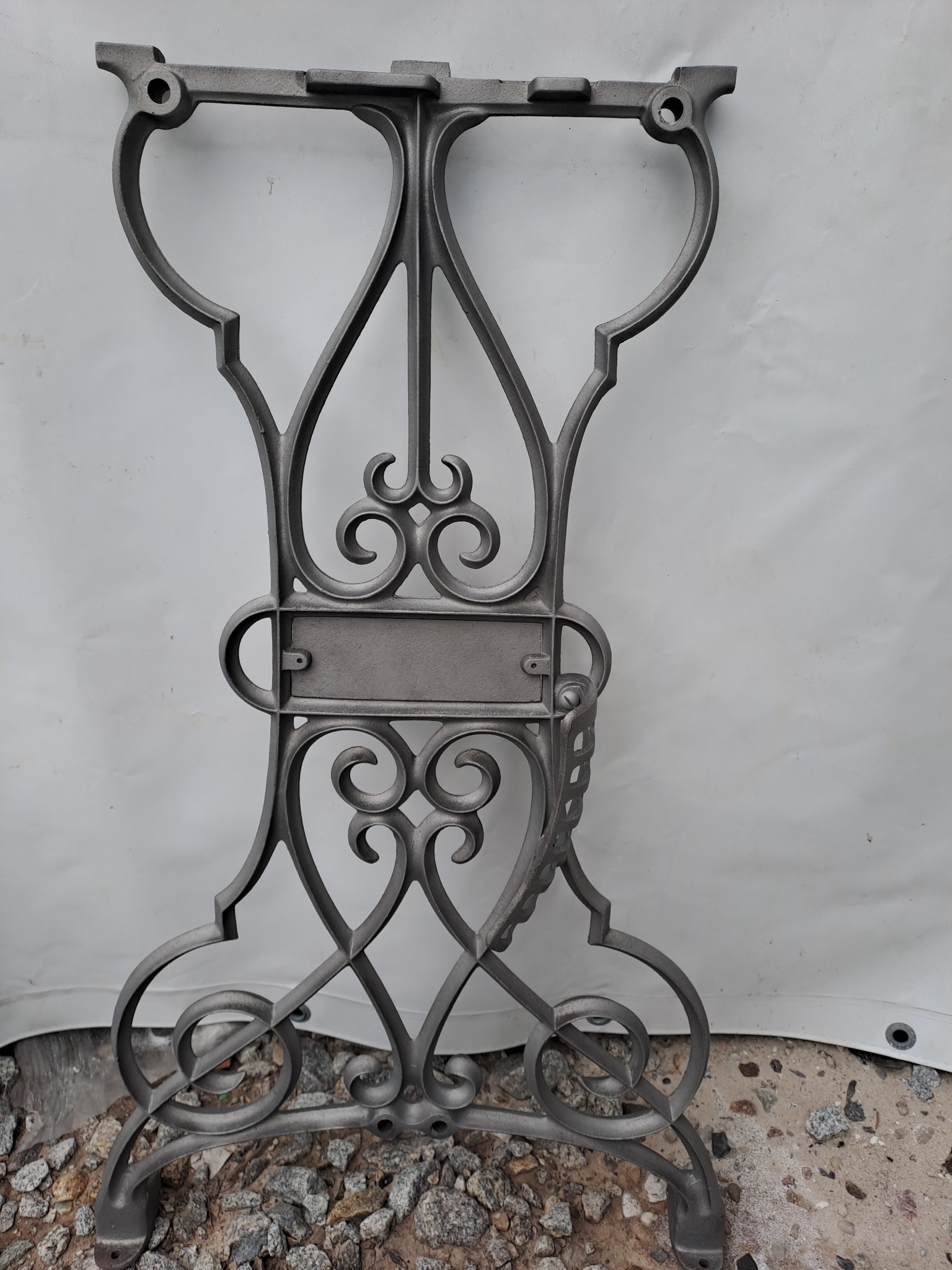 Metalowy, ozdobny stelaż stołu po obróbce, z widoczną drobną fakturą powierzchni, na tle białej plandeki i gruzu.