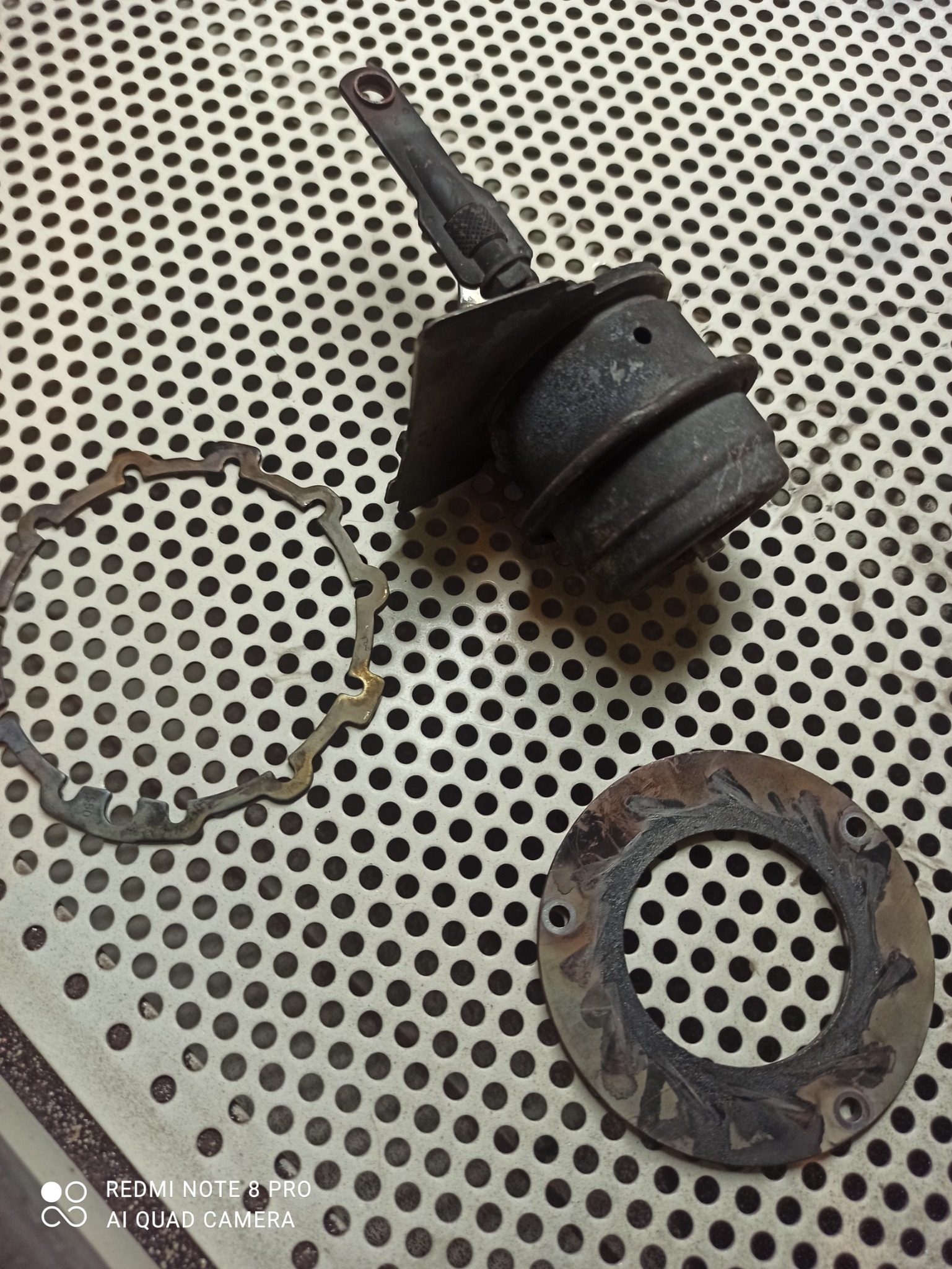 Elementy metalowe, w tym obejma i uszczelki, po procesie czyszczenia na perforowanym metalowym blacie.