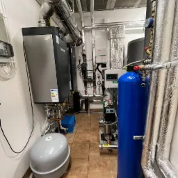 Kompletna instalacja z pompą ciepła i zbiornikiem buforowym w kotłowni w Namysłowie, widoczne liczne rury i zawory.