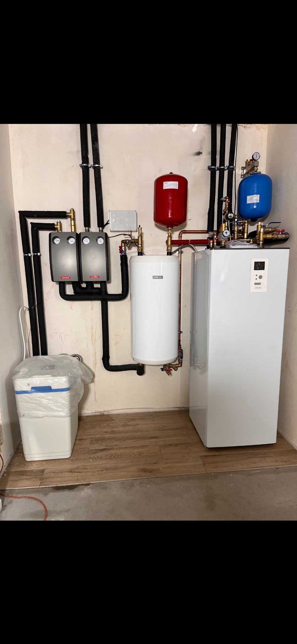 Kompletny system grzewczy w kotłowni: biały piec, zbiornik buforowy, naczynia wzbiorcze (czerwone i niebieskie), dwa moduły sterujące Onnline oraz zmiękczacz wody w folii ochronnej.