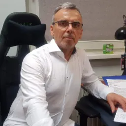 Mężczyzna w okularach siedzi przy biurku w czarnym fotelu Razer, przeglądając dokumenty.