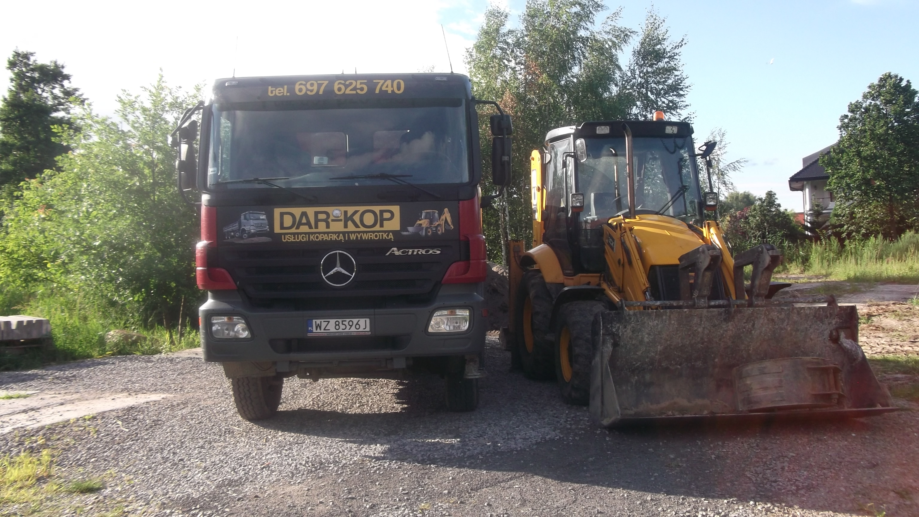Żółta koparko-ładowarka i ciężarówka Mercedes Actros firmy DAR-KOP z numerem telefonu 697 625 740 na tle zieleni i domu.