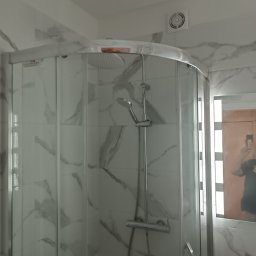 REM-RYS - Nowoczesna kabina prysznicowa narożna z chromowanymi profilami i deszczownicą, wykończona płytkami imitującymi marmur, z widoczną kratką wentylacyjną na suficie i odbiciem osoby robiącej zdjęcie...