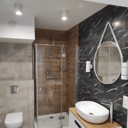 Bud-Mar - Nowoczesna łazienka z kabiną prysznicową, umywalką nablatową na drewnianym blacie, okrągłym lustrem z białym obramowaniem i czarno-białą marmurową ścianą.