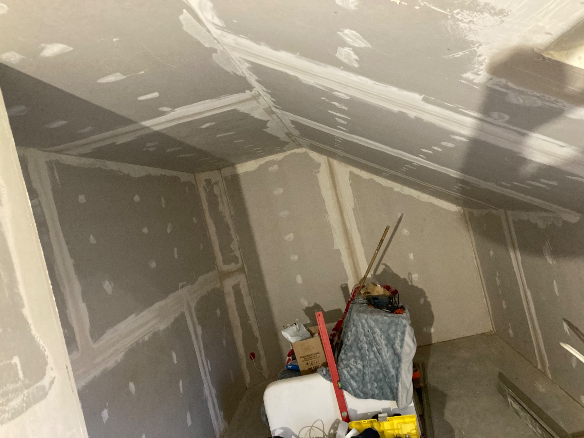 Poddasze w trakcie wykańczania płytami kartonowo-gipsowymi, widoczne łączenia płyt zaszpachlowane, na podłodze narzędzia i materiały budowlane, w tle ukośny sufit.