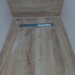 Mieczkowski Budownictwo - Płytki podłogowe imitujące drewno w kabinie prysznicowej z odpływem liniowym, jasne fugi.