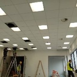 Multifinish - Montaż sufitu podwieszanego w jasnym pomieszczeniu biurowym; widoczne kwadratowe panele sufitowe, otwory wentylacyjne oraz pracownicy na drabinach.