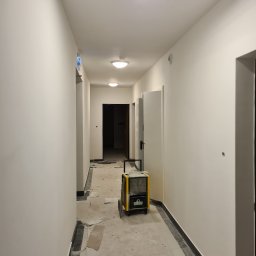 Multifinish - Korytarz w trakcie prac wykończeniowych; świeżo pomalowane, gładkie ściany, na podłodze resztki materiałów budowlanych, widoczny osuszacz powietrza.
