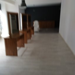 Multifinish - Wnętrze lokalu usługowego w trakcie wykańczania, widoczne drewniane biurka z lustrami w rzędzie, szara podłoga imitująca drewno, czarna ściana w tle i białe ściany boczne, surowa lampa wisząca.