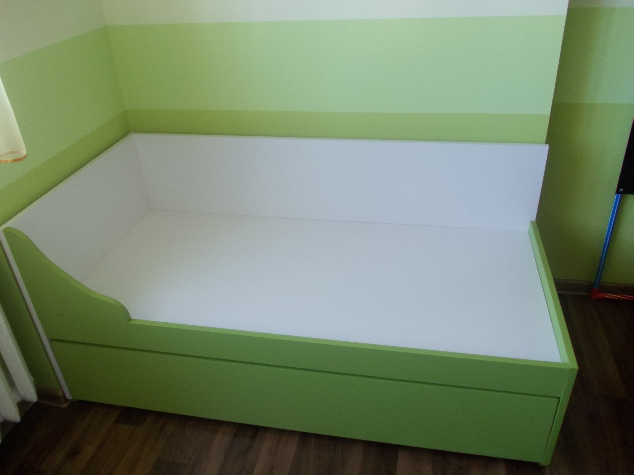 Narożne łóżko dziecięce z szufladami w kolorze zielonym, dopasowane do dwukolorowej ściany w pokoju, widok z niskiego kąta.