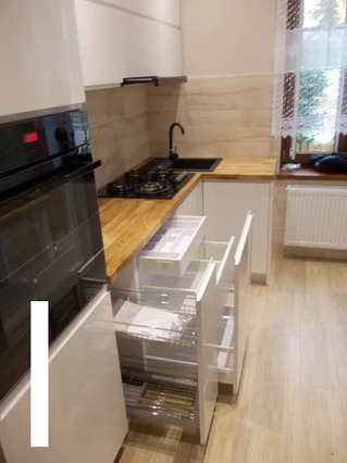 Nowoczesna biała kuchnia z drewnianym blatem, czarną armaturą i otwartymi szufladami cargo z metalowymi koszami.