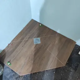 Układanie drewnopodobnych płytek w rogu łazienki, widoczny odpływ liniowy i poziomujące klipsy, jasnoniebieskie ściany.