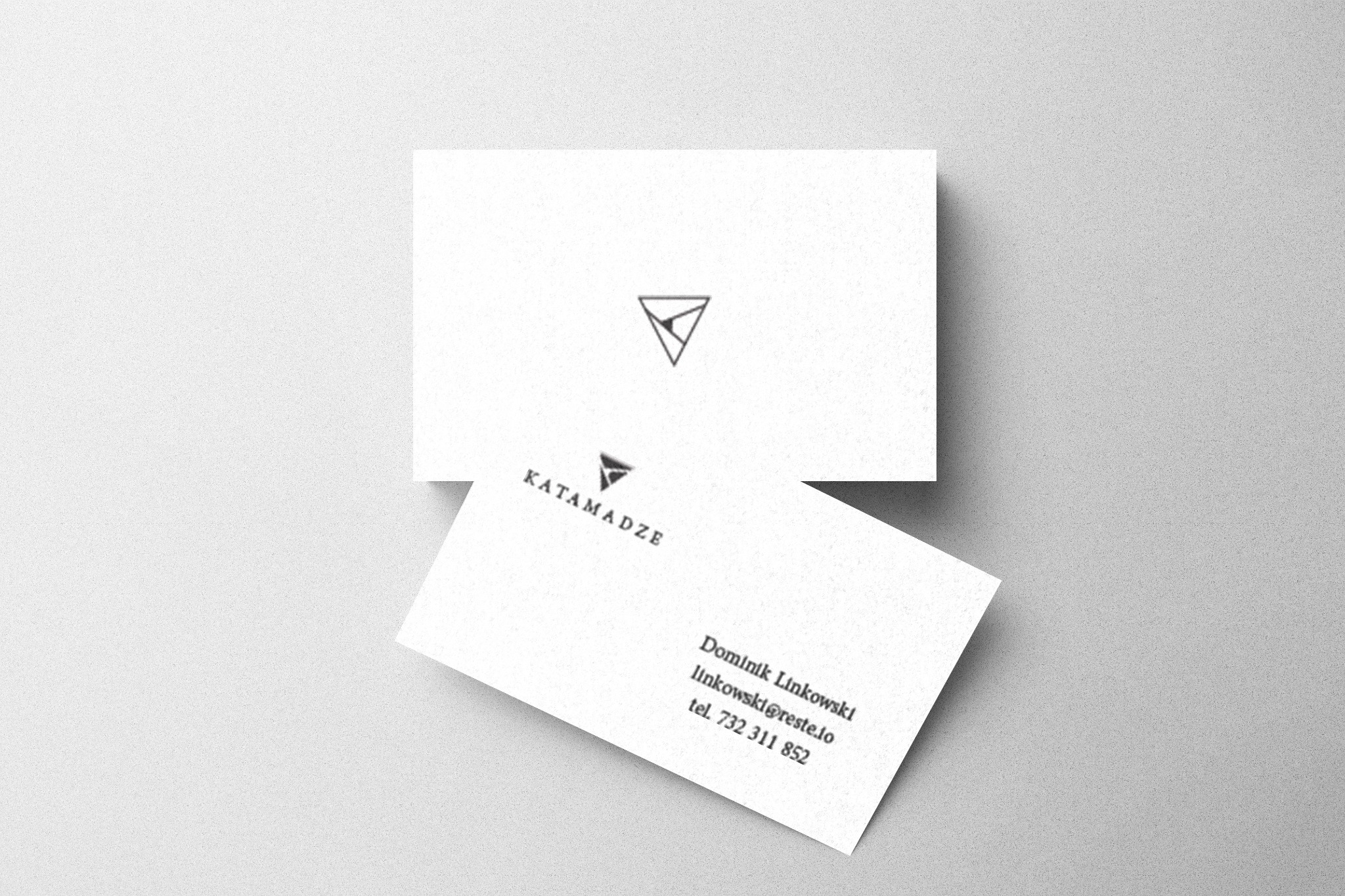 Dwie białe wizytówki z minimalistycznym logo i danymi kontaktowymi ułożone na jasnoszarym tle, górna wizytówka lekko przesunięta ku górze.
