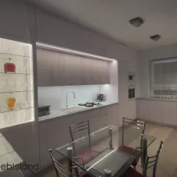 Nowoczesna kuchnia z białymi frontami i drewnopodobnymi szafkami górnymi, oświetleniem LED podszafkowym i przeszkloną witryną z dekoracyjnym szkłem i butelkami, widoczny stół z szklanym blatem.