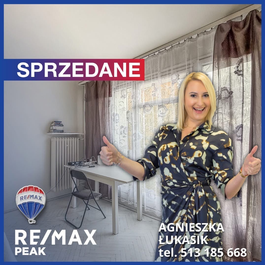 Uśmiechnięta blondynka z RE/MAX Peak prezentuje sprzedane mieszkanie, pokazując kciuki w górę. W tle pokój z oknem i napisem 'SPRZEDANE'.