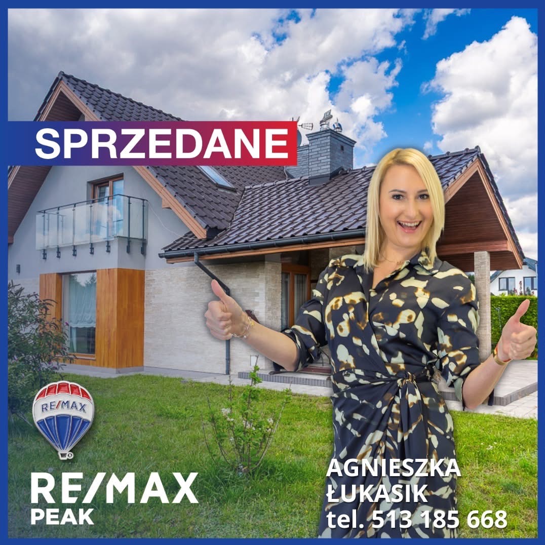 Uśmiechnięta blondynka z podniesionymi kciukami na tle domu z napisem 'Sprzedane' i logo RE/MAX, sugerująca udaną transakcję nieruchomości.