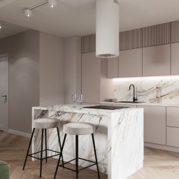 InterSpace Design - Nowoczesna kuchnia z wyspą wykończoną marmurem, minimalistycznymi szafkami w odcieniach beżu i drewnianą podłogą w jodełkę. Nad wyspą zawieszony cylindryczny okap.