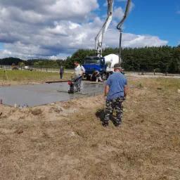 Wylewka betonowa wykonywana w Warce. Widoczny pracownik obsługujący maszynę do wygładzania betonu, pompa do betonu oraz świeżo wylany beton.