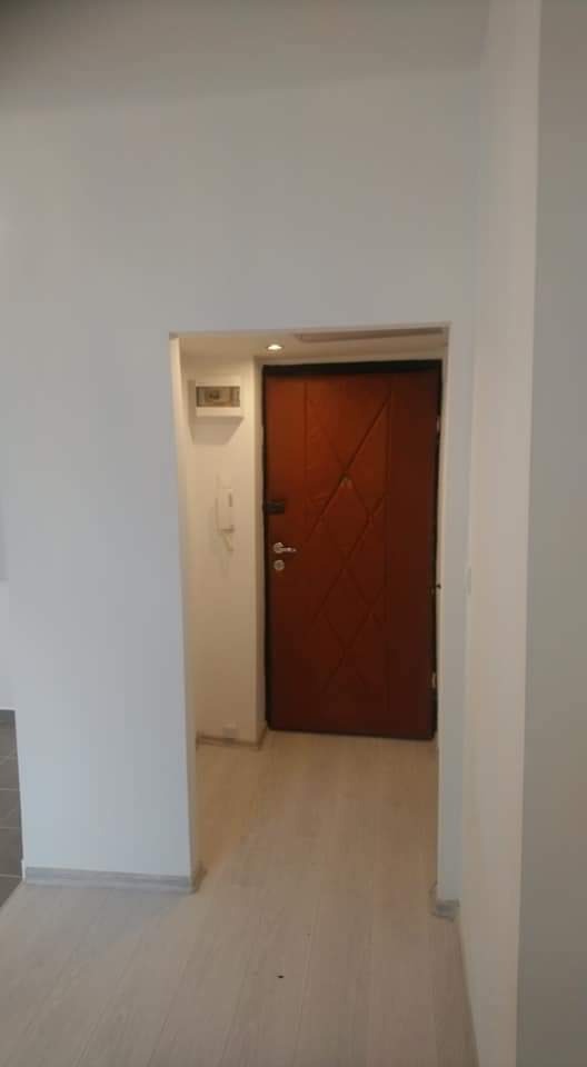 Wnętrze po odświeżeniu: Jasne ściany, drewnopodobne panele podłogowe i ciemne drzwi wejściowe z geometrycznym wzorem.