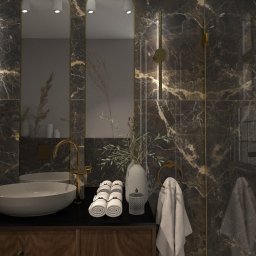 Dominika Chabiniak IDEAA - Elegancka łazienka z ciemnymi marmurowymi płytkami, złota armatura, owalna umywalka nablatowa, dekoracyjne oświetlenie i białe ręczniki.