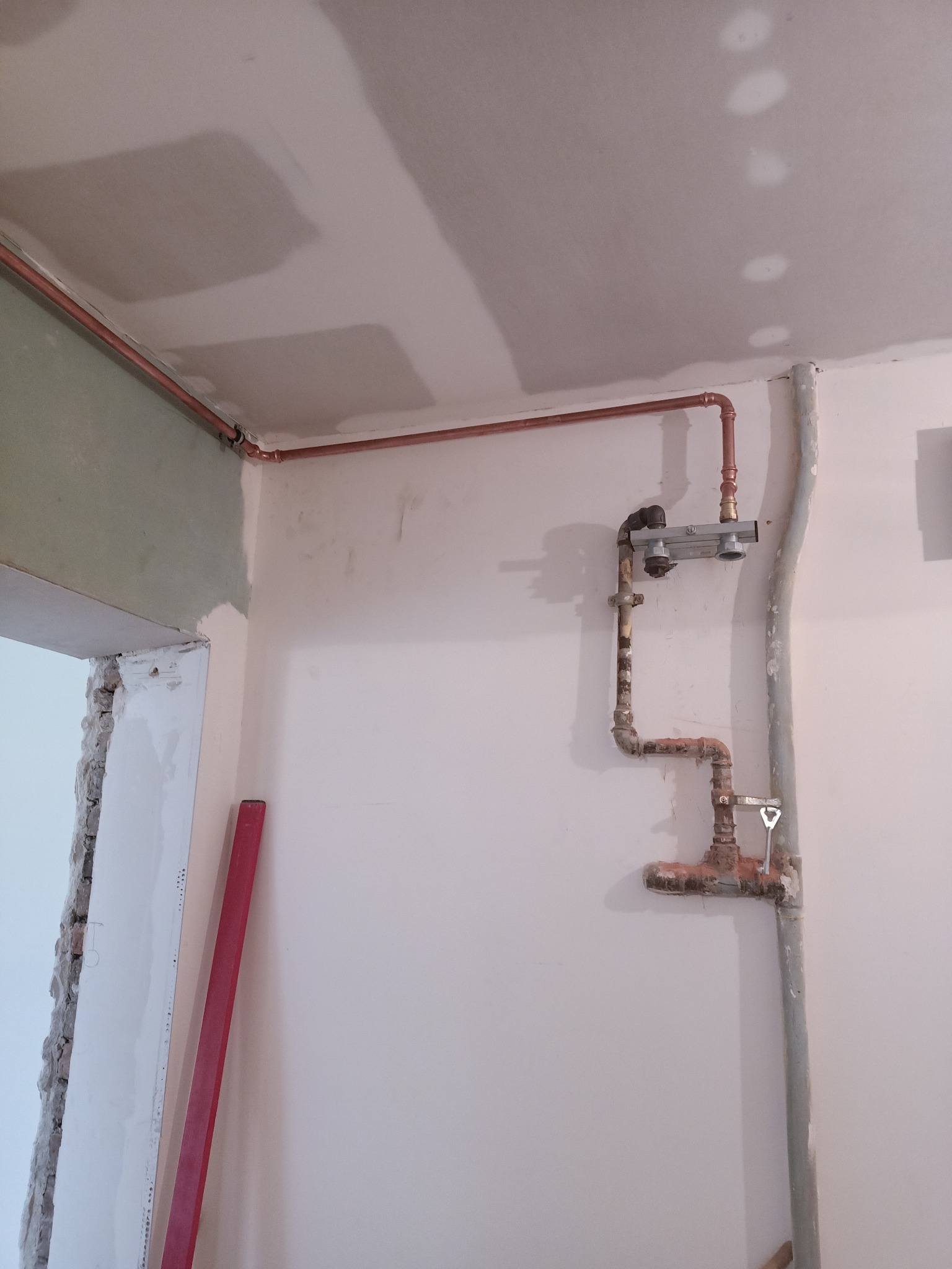 Fragment instalacji grzewczej z miedzianymi rurami w surowym stanie w Szczecinie, widoczne połączenia i zawory, ściany w trakcie wykończenia.