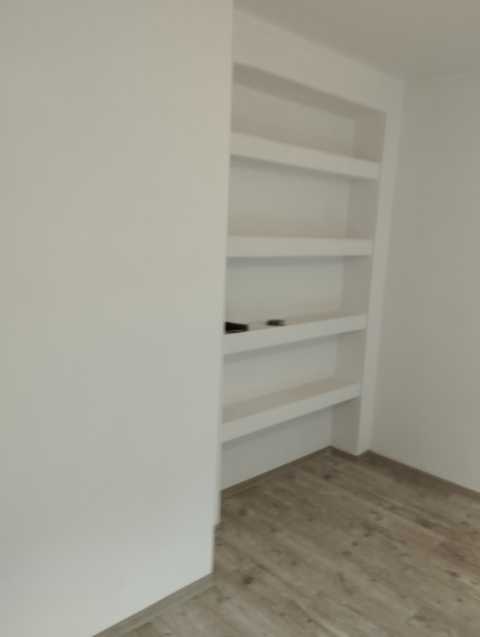 Wnęka z półkami w ścianie, wykończona na biało, podłoga z paneli imitujących drewno, minimalistyczny design.