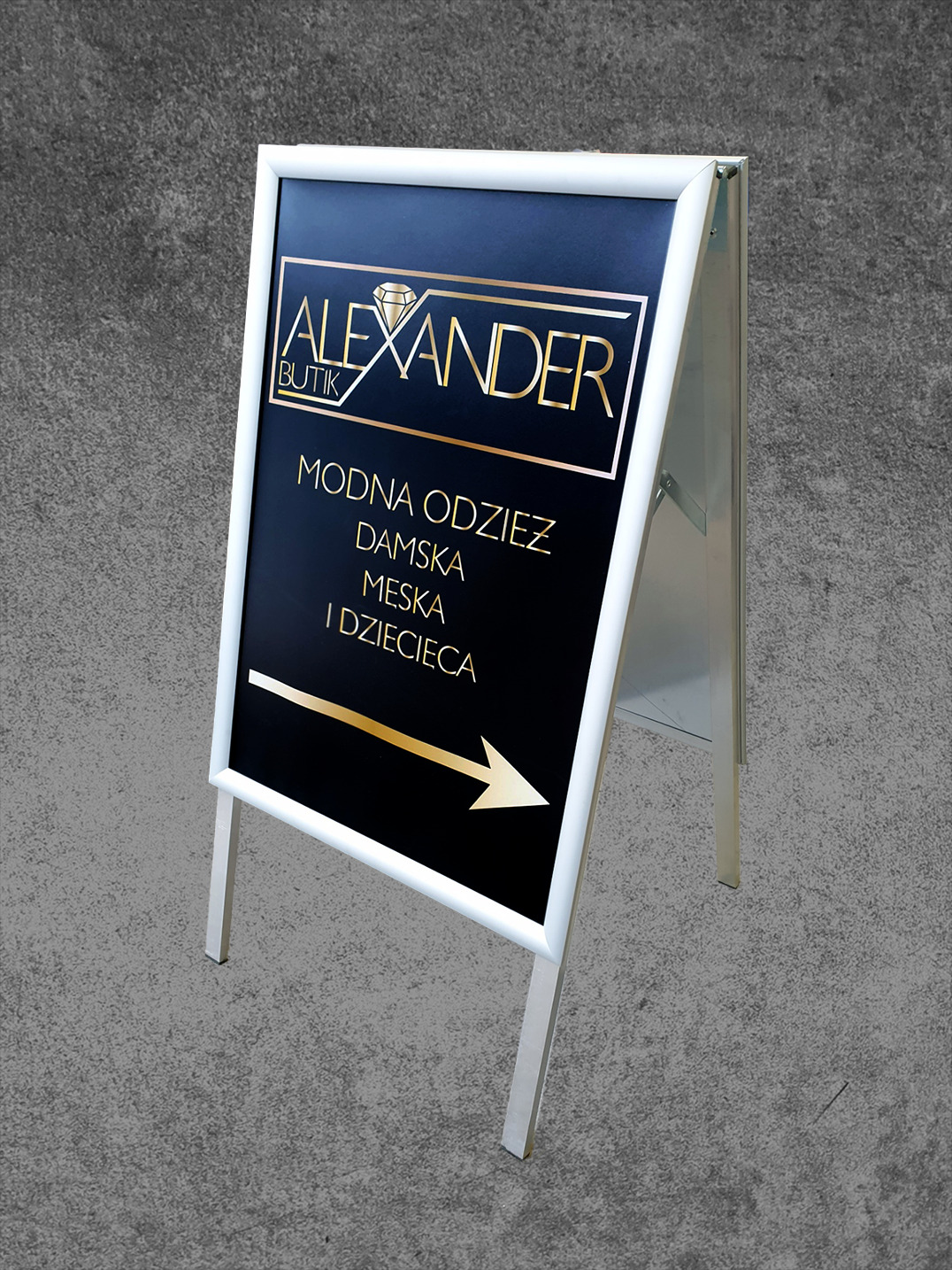 Biały potykacz reklamowy z czarnym tłem, złotym logo 'Alexander Butik', informacją o modnej odzieży damskiej, męskiej i dziecięcej oraz złotą strzałką wskazującą kierunek.