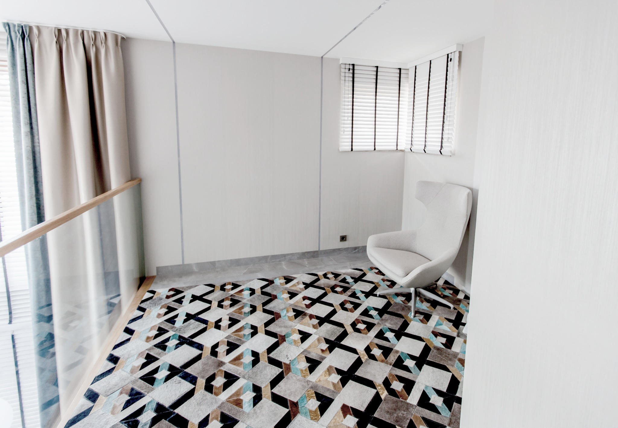 Jasne wnętrze z geometrycznym dywanem, białym fotelem i zasłoniętym oknem z żaluzjami.