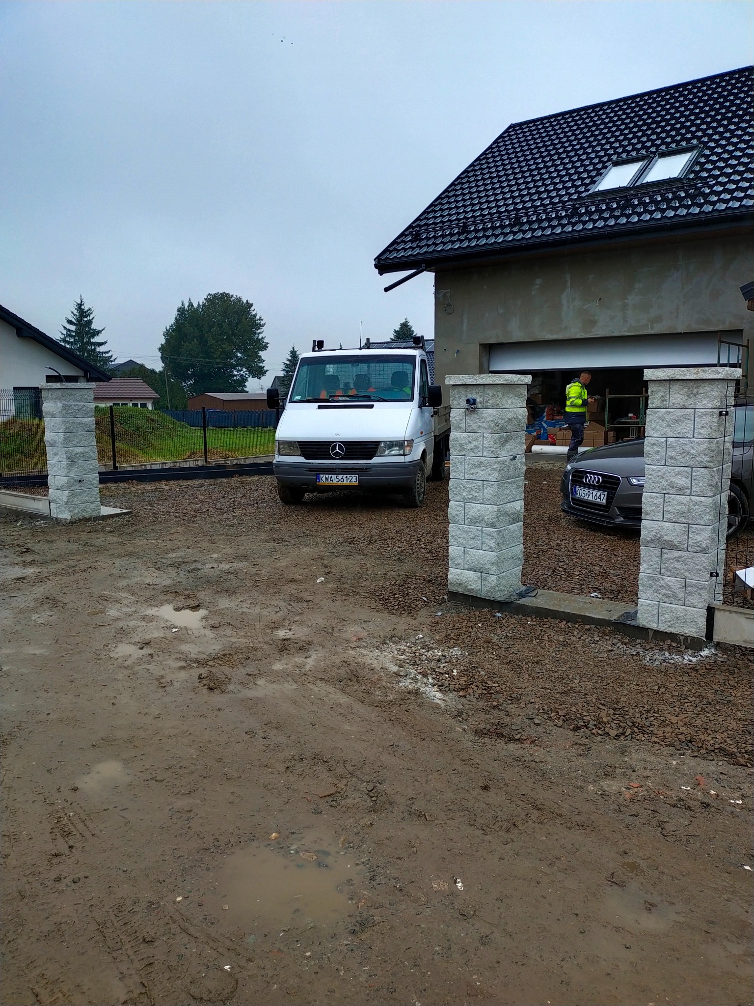 Nowo postawiona brama z kamiennymi słupkami w Spytkowicach, widok na posesję z samochodem dostawczym i osobowym w tle, teren po budowie w trakcie porządkowania.