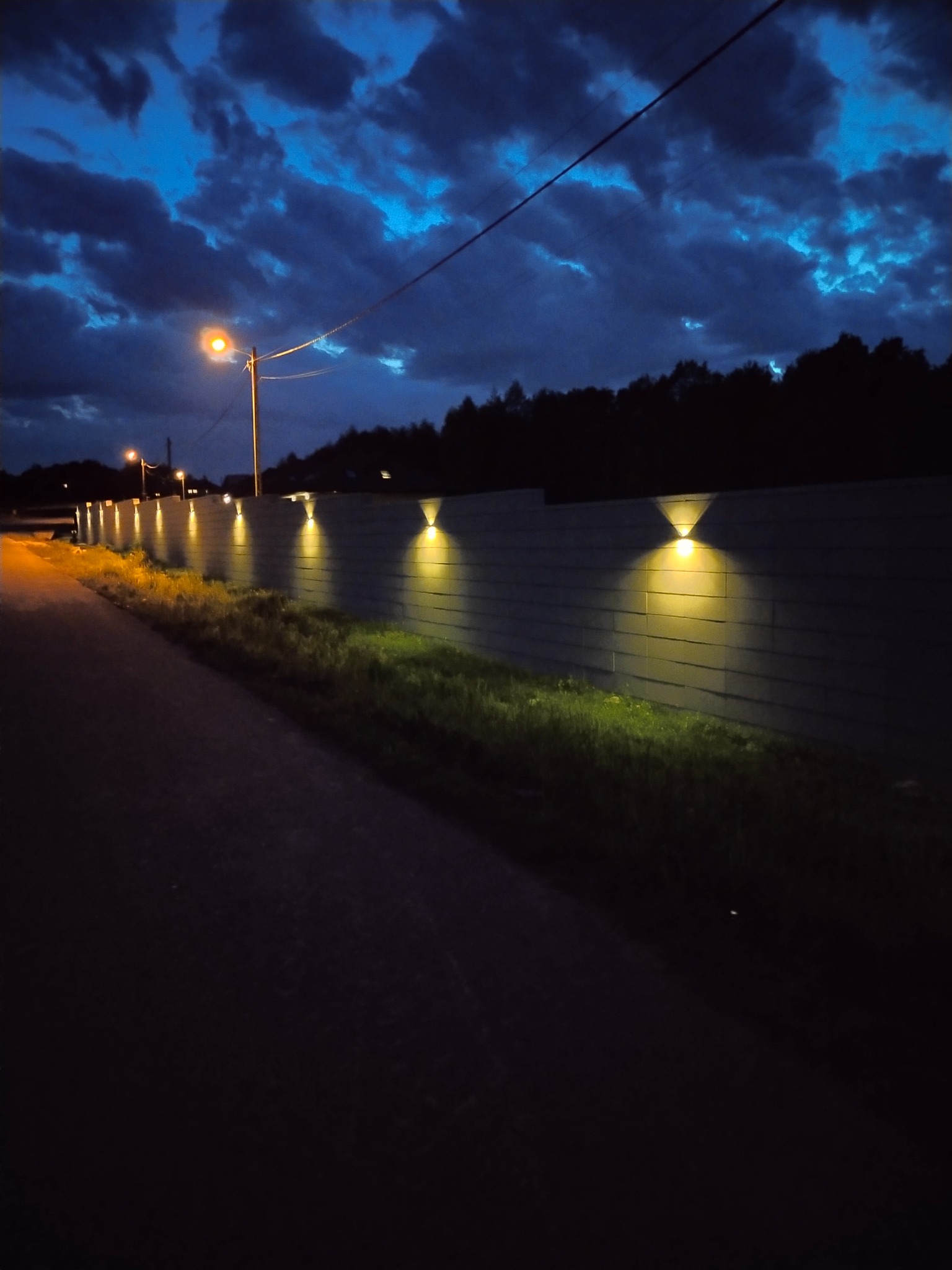 Nowoczesne ogrodzenie panelowe z oświetleniem punktowym wzdłuż ścieżki, nocne ujęcie.