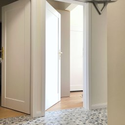 YURAX GROUP Sp. z o. o. - Wykończony korytarz z białymi drzwiami z złotymi klamkami i wzorzystą, niebiesko-białą podłogą z płytek, widoczne logo firmy na ścianie.