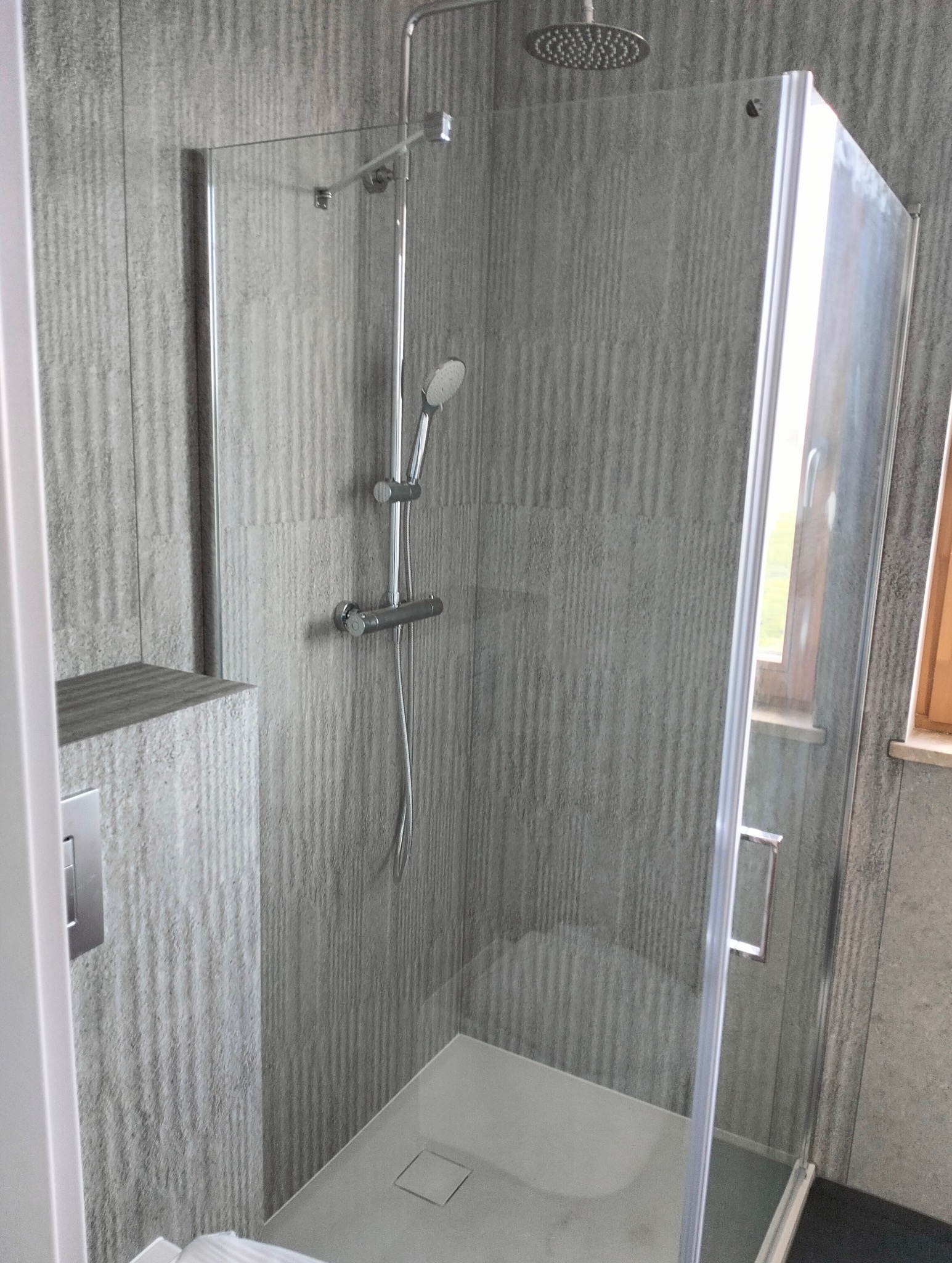 Nowoczesna kabina prysznicowa z deszczownicą i słuchawką, szare płytki imitujące drewno, minimalistyczny design.