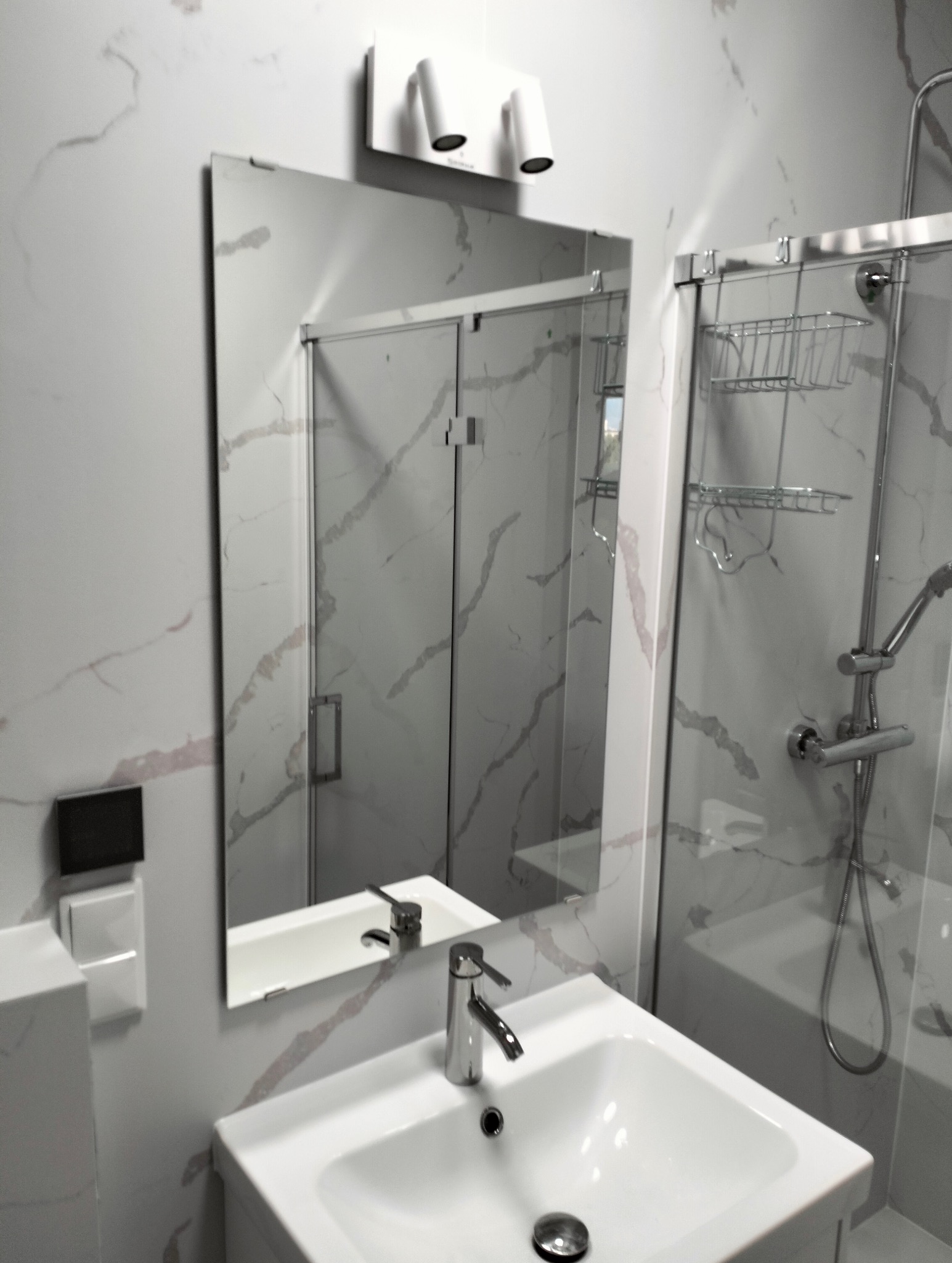 Nowoczesna łazienka z umywalką nablatową, baterią chromowaną i kabiną prysznicową za lustrem, ściany wykończone płytkami imitującymi marmur.