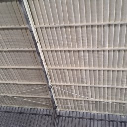 Pimar Izolacje S.C - Wnętrze hali z ocieplonym pianką PUR dachem, widoczne metalowe elementy konstrukcyjne i równomiernie nałożona warstwa izolacji w kolorze kremowym.