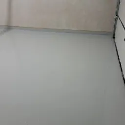 Świeżo wylana, jasnoszara posadzka w garażu, widoczna brama garażowa z czarnym uchwytem i fragment ściany w tle.