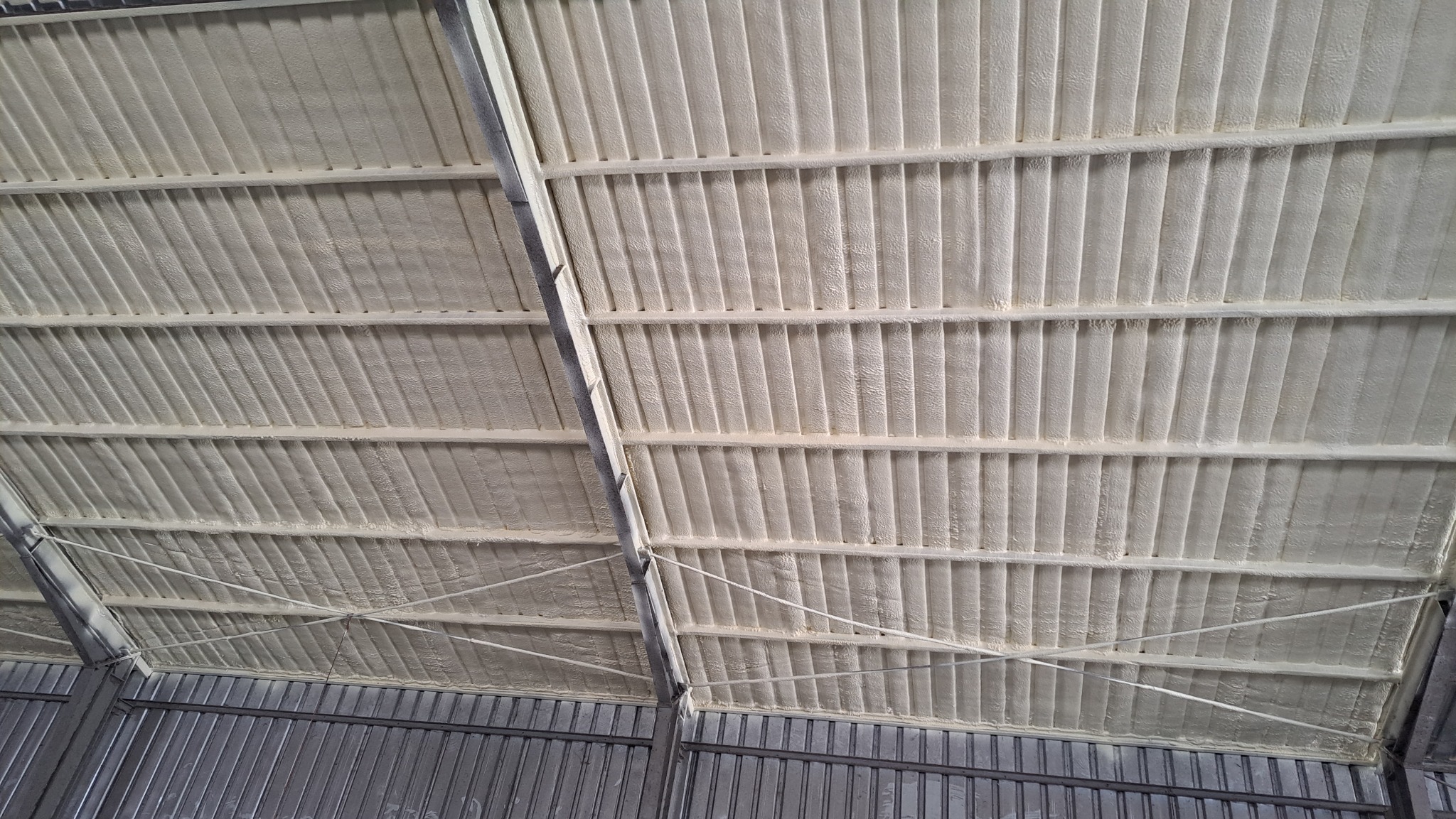 Wnętrze hali z ocieplonym pianką PUR dachem, widoczne metalowe elementy konstrukcyjne i równomiernie nałożona warstwa izolacji w kolorze kremowym.