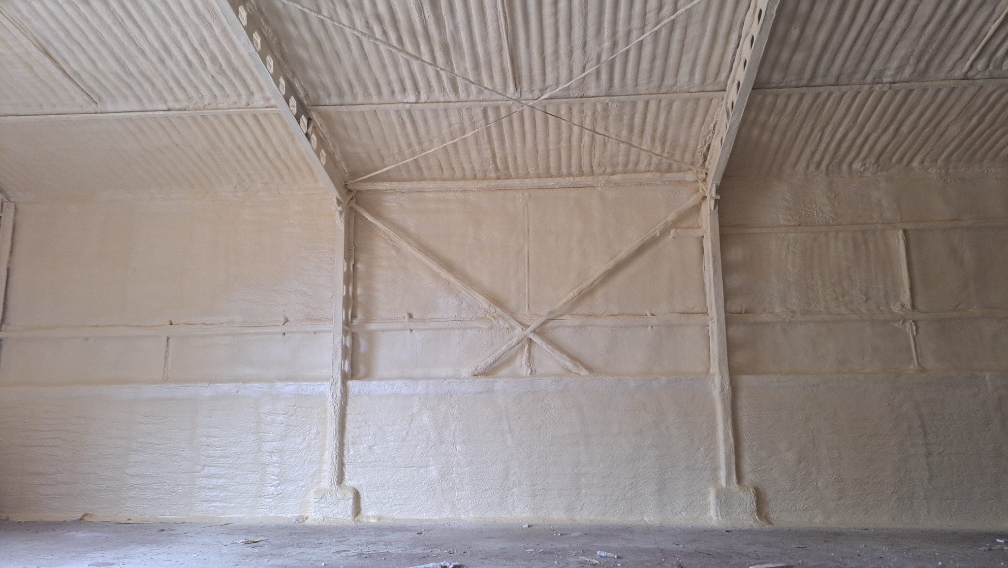 Wnętrze hali przemysłowej po natrysku izolacji pianką na ściany i dach, widoczne stalowe elementy konstrukcyjne pokryte pianą, nierówna powierzchnia izolacji.