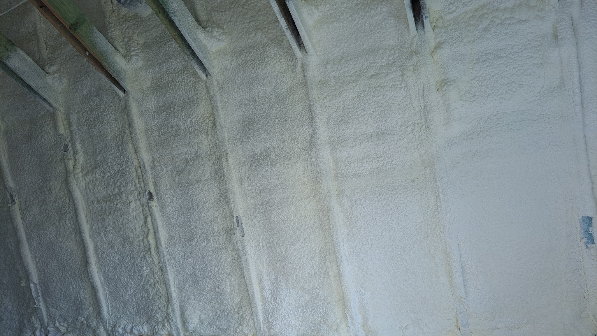 Poddasze z drewnianą konstrukcją krokwi pokryte grubą warstwą jasnej pianki izolacyjnej o nieregularnej fakturze.