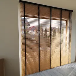 Jasne, poziome lamele okienne z czarnymi taśmami dekoracyjnymi, widok na domy przez okno.