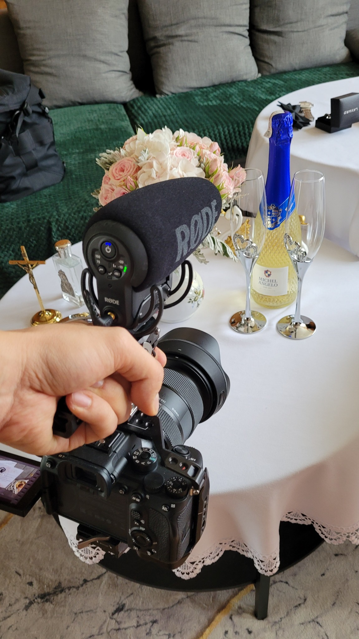 Kamera z mikrofonem Rode nagrywająca kadr z bukietem kwiatów, szampanem i kieliszkami na stole podczas uroczystości.