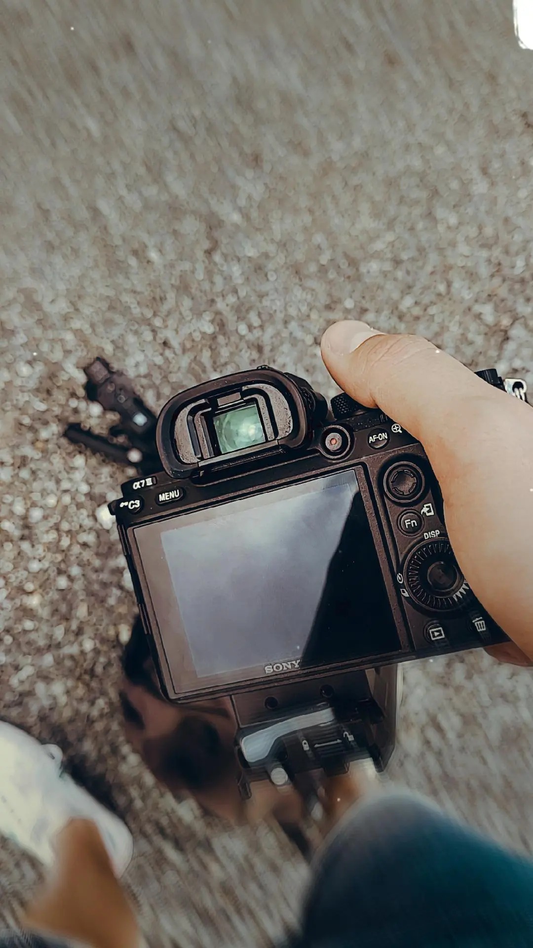 Czarny aparat Sony alfa z obiektywem i mikrofonem na statywie trzymany w dłoni na tle betonowej powierzchni.