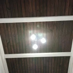 Drewniany sufit z ciemnego drewna, wykończony białymi belkami, oświetlony nowoczesną lampą z trzema kloszami.