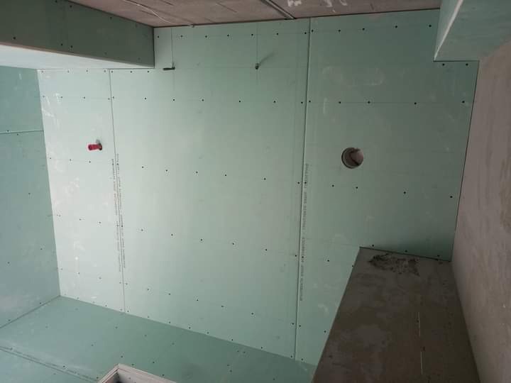 Montaż zielonych płyt gipsowo-kartonowych na ścianach i suficie w pomieszczeniu, widoczne ślady po szpachlowaniu i otwór na instalację.