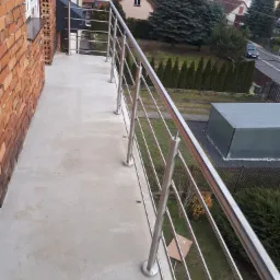 Balkon z prostą, nowoczesną balustradą ze stali nierdzewnej, widok z góry na posesję z zielonym trawnikiem i zabudowaniami gospodarczymi.