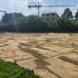 SETA-BUD sp. z o.o. - Przygotowany teren pod budowę z wykopami pod fundamenty, w tle budynek w stanie surowym i żurawie budowlane.