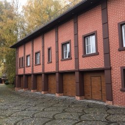 SETA-BUD sp. z o.o. - Dwukondygnacyjny budynek z czerwonej cegły z brązowymi akcentami i kilkoma bramami garażowymi, wykończony brukowaną nawierzchnią.