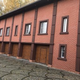 SETA-BUD sp. z o.o. - Dwukondygnacyjny budynek z czerwonej cegły z brązowymi detalami, posiadający szereg bram garażowych i okien, otoczony kostką brukową i drzewami z jesiennymi liśćmi.